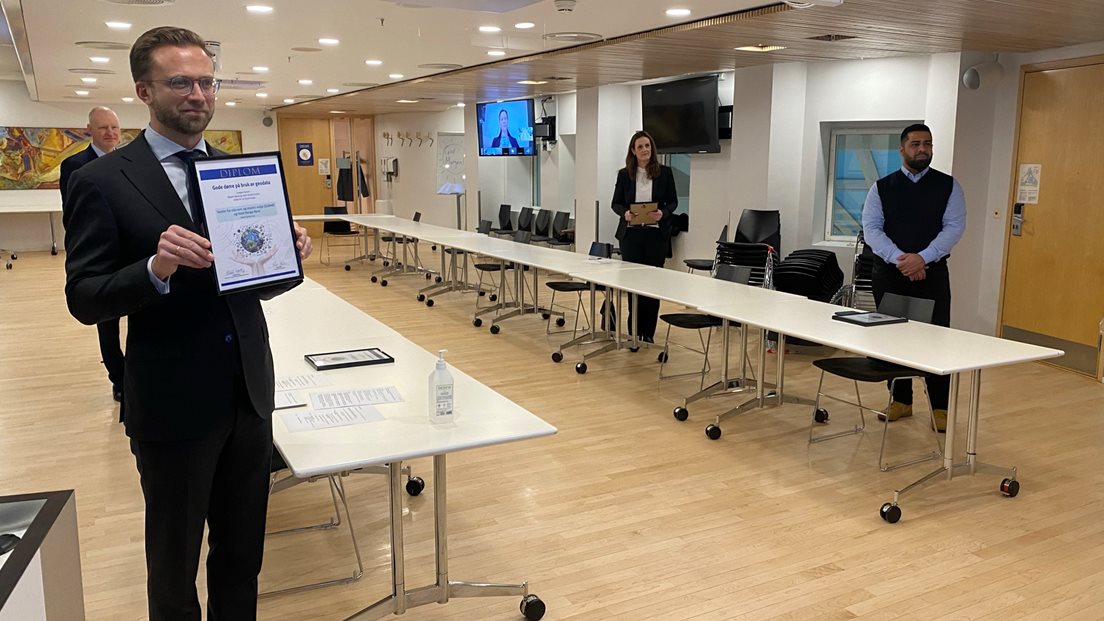 Kommunal- og moderniseringsminister Nikolai Astrup i møterom syner fram diplomet til kamera