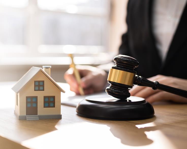 En liten modell av et hus og ei dommerklubbe i forgrunnen, med en uskarp person bak som sitter og skriver. Foto: Most Photos