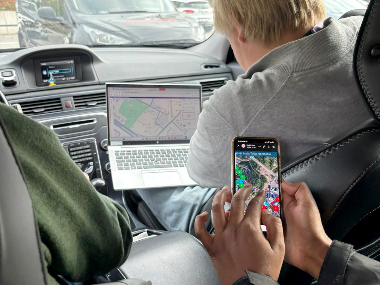 En person bruker en b&aelig;rbar PC med kart p&aring; skjermen i baksetet av en bil, mens en annen holder en mobil med et kart p&aring; skjermen. Sj&aring;f&oslash;ren ser p&aring; veien.