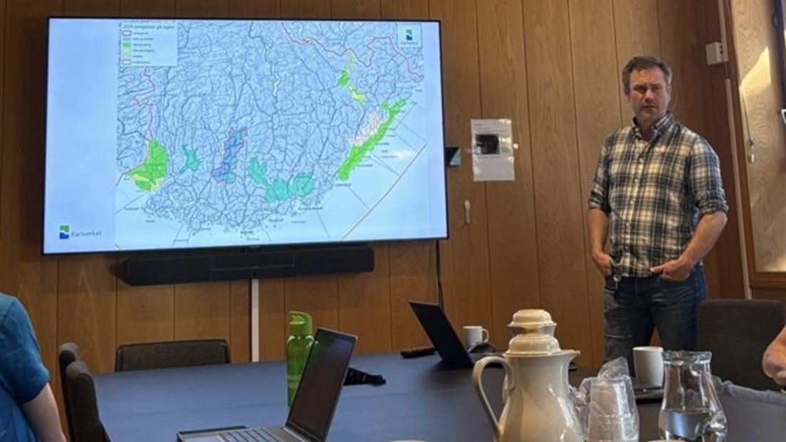 Mann står og snakker foran en storskjem der et kart vises