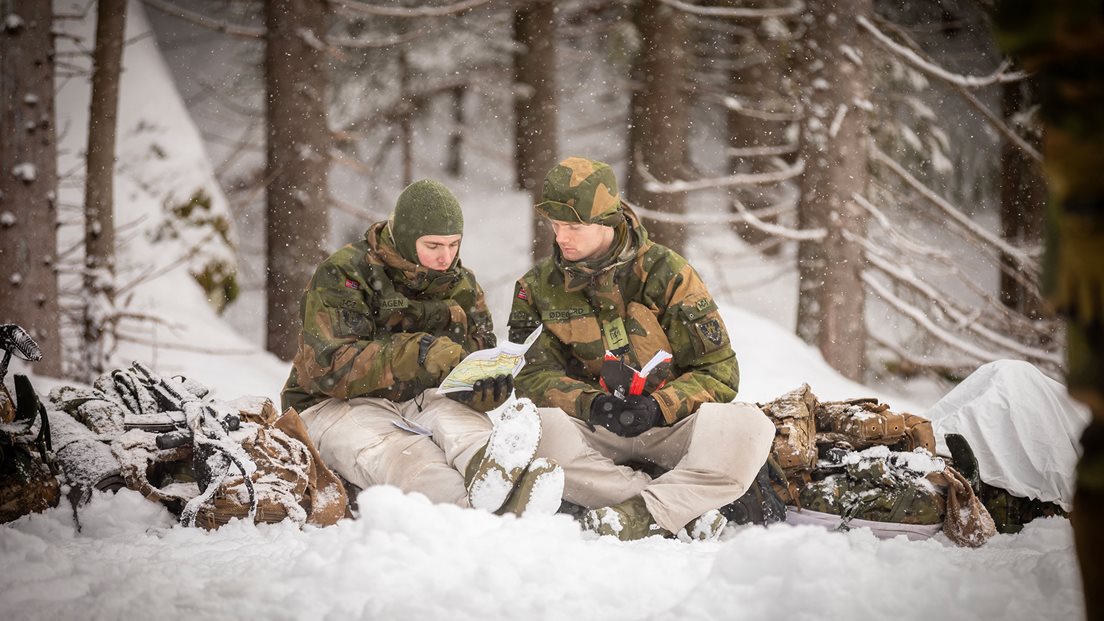 To soldater sitter i vinterskog på en pulk og kikker på kart