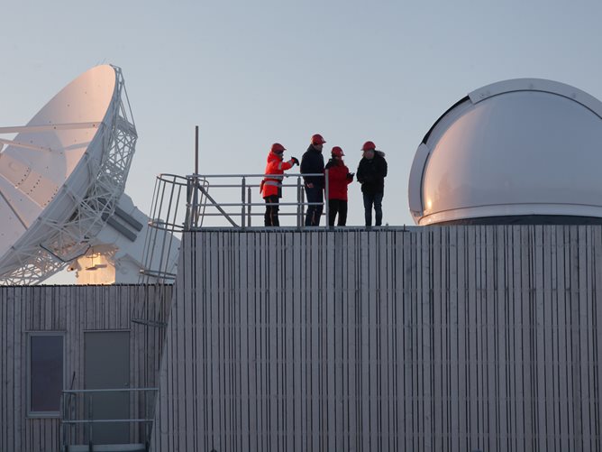 Personer på taket ved satellittavstandsmaler ved Kartverkets jordobservatorium i Ny-Ålesund