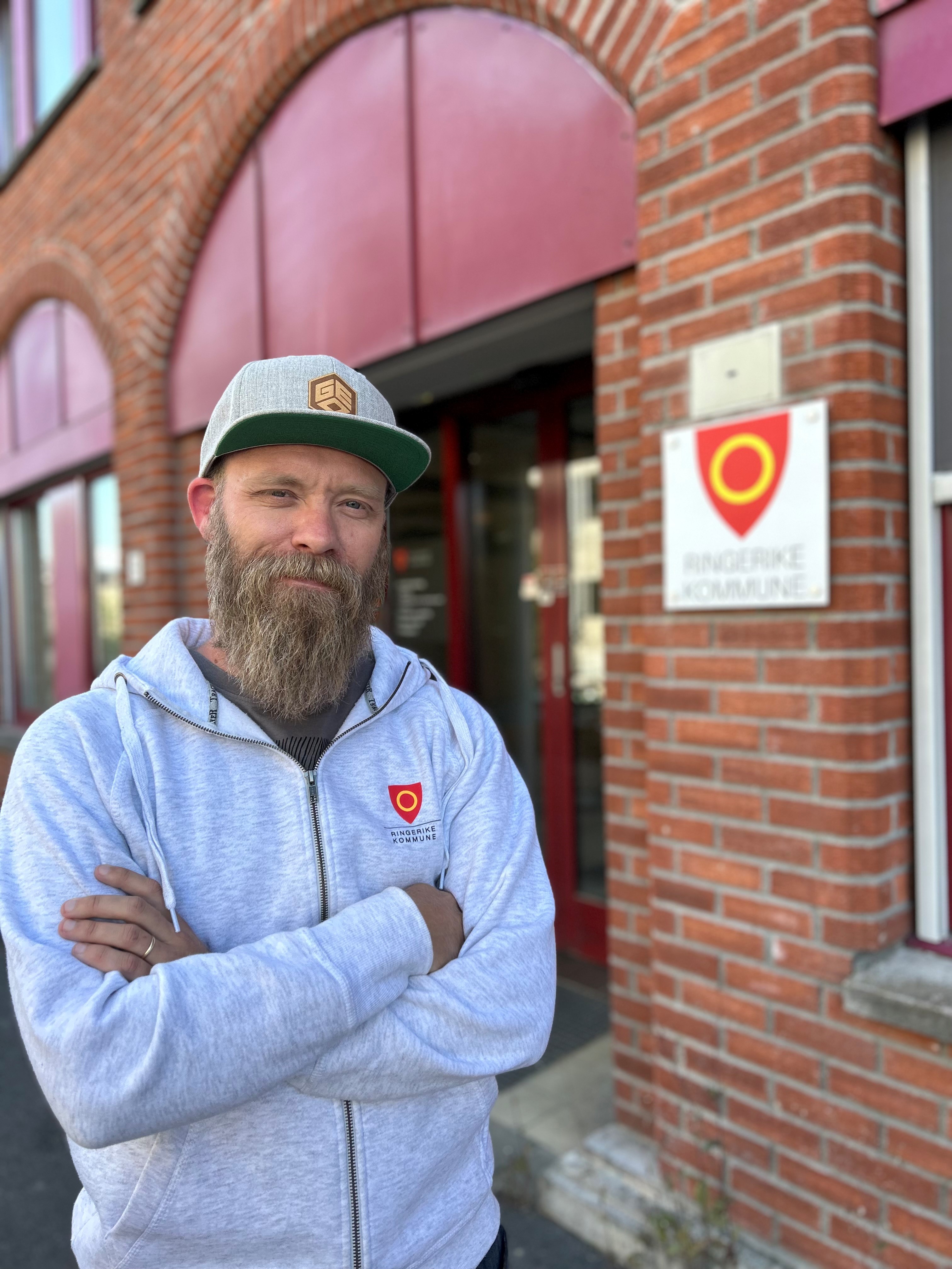 Mann med skjegg foran bygning med skilt til Ringerike kommune.