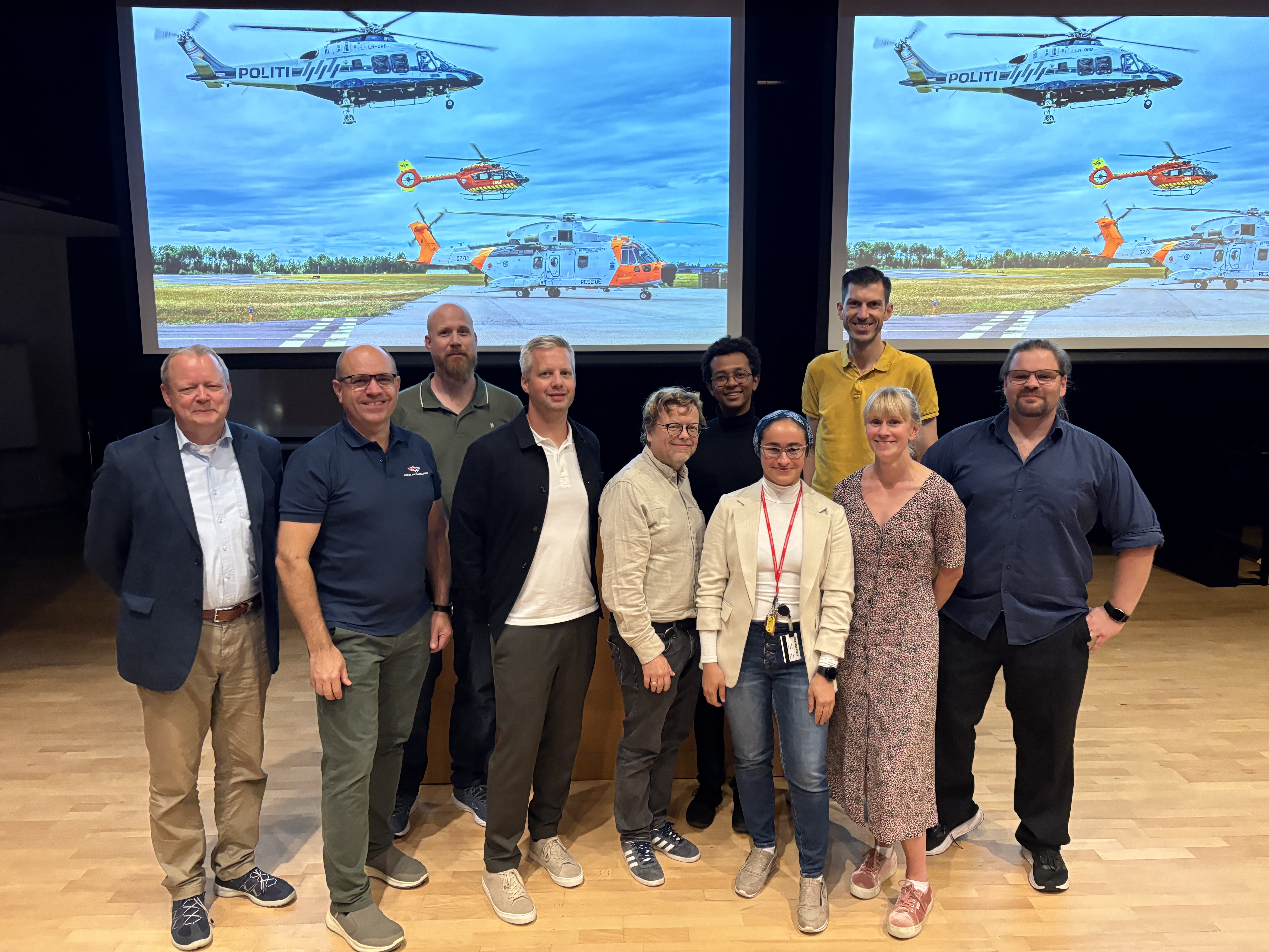 Ti menneseker samla p&aring; en scene foran to storskjermer som viser beredskapshelikopter.