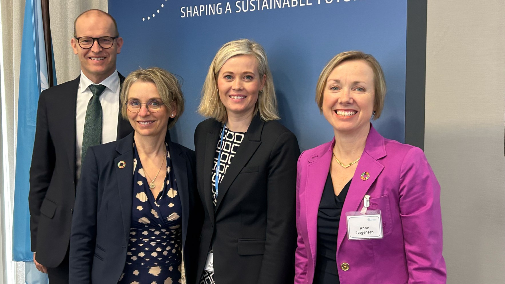 &Eacute;n mann og tre kvinner smiler. Alle er kledd formelt.