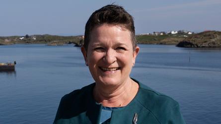 Birte Noer Borrevik med kystlandskap i bakgrunnen.