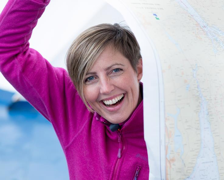 Smilende dame med kort hår og rosa jakke holder et papirsjøkart delvis over hode og kropp. Foto: Morten Brun