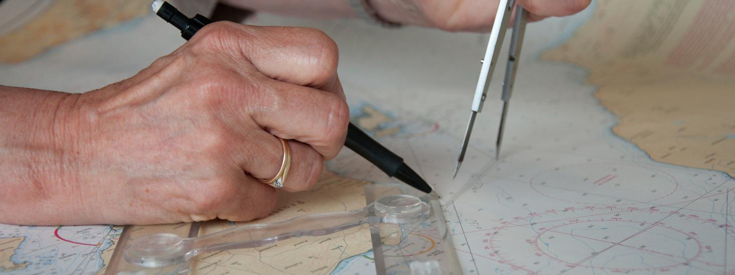 Hender plotter inn rettelse i sjøkart ved hjelp av paralellfoskyver, passer og blyant. Foto.