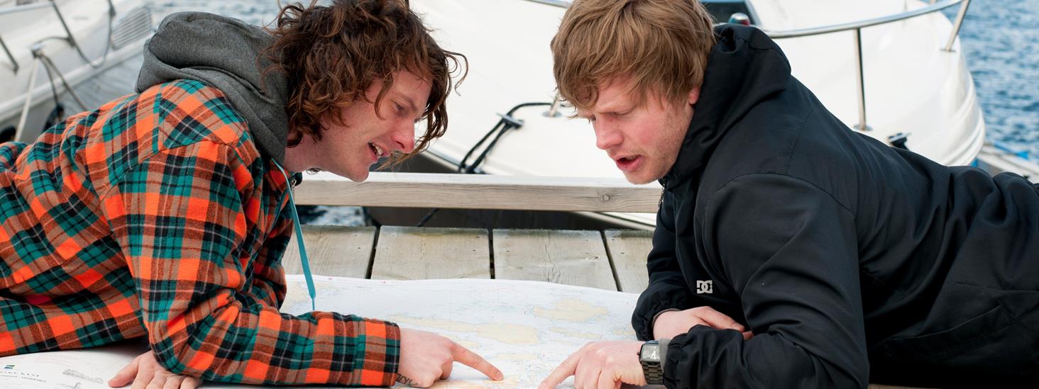 To menn ligger på brygga i ei småbåthavn og peker i et sjøkart. Foto: Morten Brun